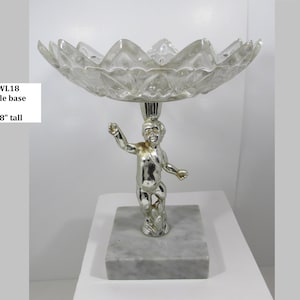 May include: A decorative centerpiece featuring a clear, petal-shaped glass bowl supported by a silver cherub figurine on a marble base. The piece is 6-7/8 inches tall. The text "BOWL18 marble base" is visible.