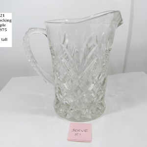 May include: Clear glass pitcher with a textured pineapple design. The pitcher has a handle and a spout. The text "SERVE21 Anchor Hocking Pineapple 1967-1975 5-3/16" tall" is visible. A pink square with "SERVE 21" is at the bottom.