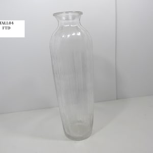 May include: A clear glass vase with a textured, vertical striped design. The vase has a tall, slender shape with a slightly flared opening. The text "TALL04 FTD" is in a white rectangle.