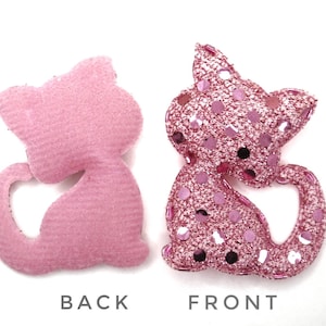 Op de afbeelding: Roze vilt en roze glitter kattenapplicatie met een hartvormige uitsparing aan de achterkant. De voorkant van de kat is bedekt met roze glitterpailletten.
