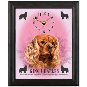 May include: A pink framed clock featuring a Cavalier King Charles Spaniel dog image. The clock face has black Roman numerals and gold hands. The text "KING CHARLES" and "A constant, patient companion with a happy and eager temperament" is below the dog image.