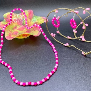 May include: A pink and light pink beaded necklace and matching earrings. The necklace is made of small round beads and is about 18 inches long. The earrings are also made of small round beads and are about 1 inch in diameter.