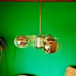 Puede incluir: Una lámpara de techo moderna de cromo y acrílico transparente con tres globos redondos. La lámpara está colgada de un techo contra una pared verde.