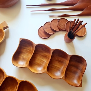 Pode incluir: Dois pratos de servir de madeira com múltiplos compartimentos. O prato maior tem a forma de uma banana e tem sete compartimentos. O prato menor tem a forma de uma onda e tem quatro compartimentos.