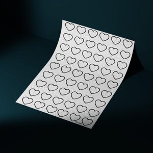Op de afbeelding: Een vel wit papier met talrijke zwarte hartomtrekken. Het papier is licht gebogen, met een opgetild hoekje, waardoor een donkerblauwe achtergrond zichtbaar wordt. De harten zijn gelijkmatig verdeeld en de rechter benedenhoek van het papier heeft de tekst "40 mm".
