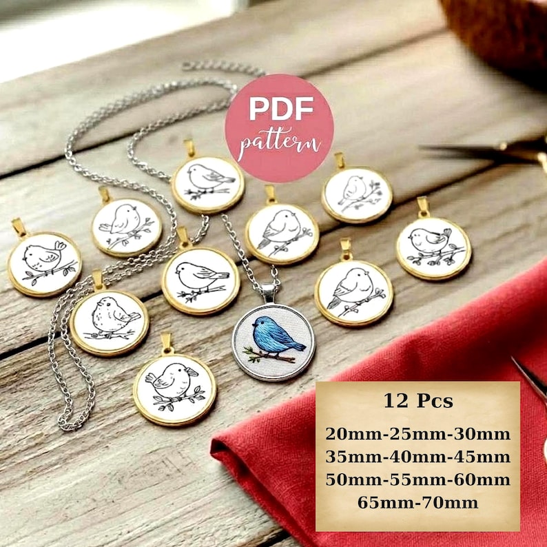 A collection of circular, gold-rimmed pendants rests on a light-colored wooden surface. Each pendant contains a different minimalist line-art illustration of a bird on a white background. In the foreground, a red fabric napkin is partially visible on the right, and a pair of vintage-style scissors lies at the top. A pink "PDF pattern" circular label and a text box indicating available sizes (20 mm to 70 mm) are overlaid on the image.