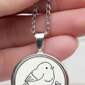 Silver necklace with a circular pendant. The pendant displays a black and white drawing of a bird on a branch. The chain is delicate and silver in colour.