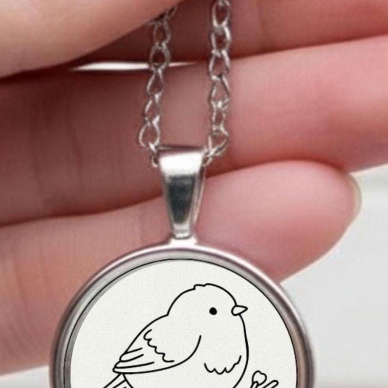 Silver necklace with a circular pendant. The pendant displays a black and white drawing of a bird on a branch. The chain is delicate and silver in colour.