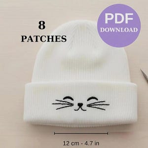 Puede incluir: Un gorro de punto blanco con un diseño de cara de gato, con bigotes y ojos bordados en negro. El gorro mide 12 cm de ancho. La imagen también incluye el texto "8 PATCHES" y un círculo morado con "PDF DOWNLOAD".