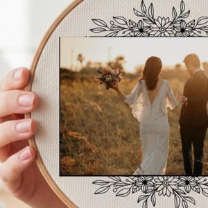 May include: A circular wooden embroidery hoop frame containing a rectangular photograph of a couple in a field. The bride wears a white lace dress and holds a bouquet, while the groom wears a dark suit. Black floral line art borders the photo.