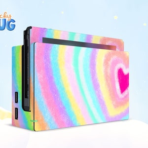 Könnte beinhalten: Eine bunte Tie-Dye-Nintendo Switch-Konsolenhaut mit einem rosafarbenen Herzdesign. Die Haut besteht aus einem strapazierfähigen Vinylmaterial und ist einfach anzubringen und zu entfernen. "Sticky Hug" ist in der oberen linken Ecke der Haut aufgedruckt.