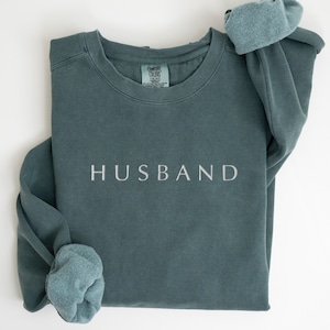 May include: A teal blue sweatshirt with the word "HUSBAND" embroidered in white on the front.