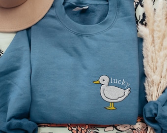 May include: A blue sweatshirt with a white embroidered duck and the word "lucky" on the front.