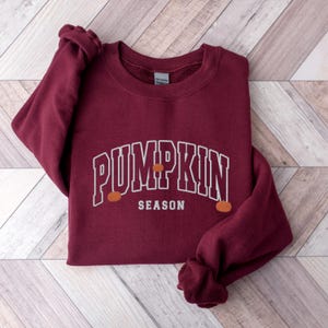 May include: Burgundy sweatshirt with white text that reads "Pumpkin Season" with three small orange pumpkins on the sweatshirt.
