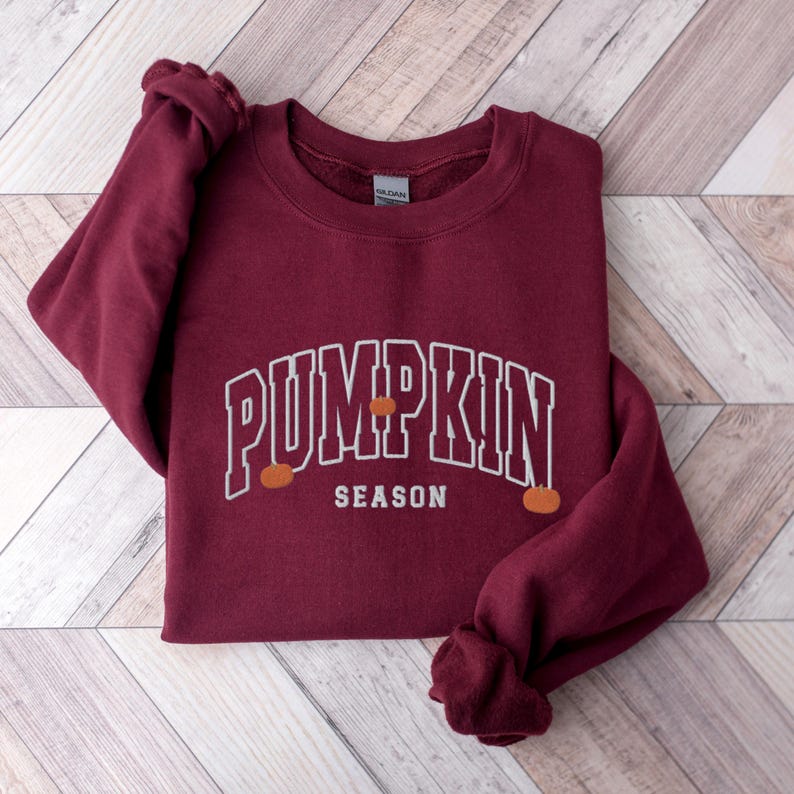 May include: Burgundy sweatshirt with white text that reads "Pumpkin Season" with three small orange pumpkins on the sweatshirt.