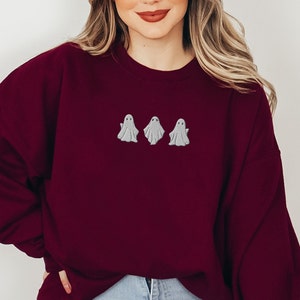 May include: A maroon sweatshirt with three embroidered white ghosts on the front.