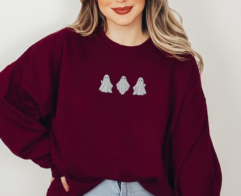May include: A maroon sweatshirt with three embroidered white ghosts on the front.