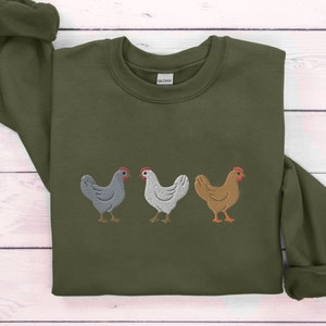 May include: A green sweatshirt with an embroidered design of three chickens in a row. The chickens are gray, white, and brown.