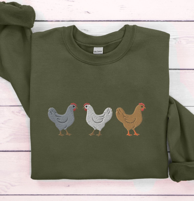 May include: A green sweatshirt with an embroidered design of three chickens in a row. The chickens are gray, white, and brown.