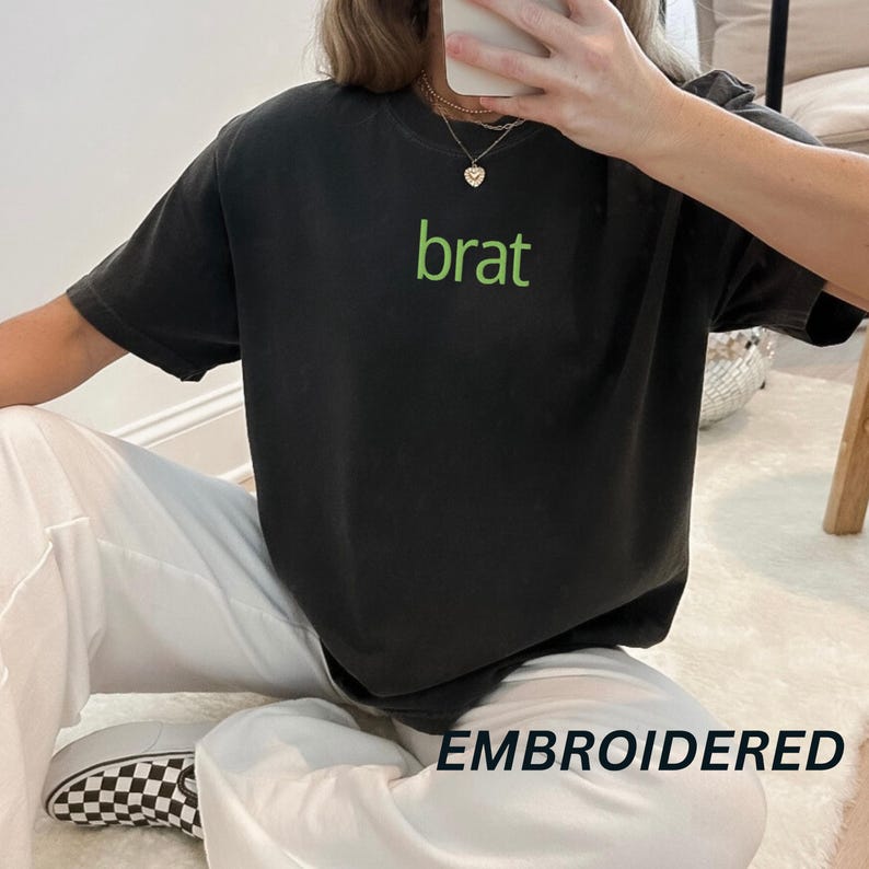 May include: Black t-shirt with green embroidered text that says "brat".