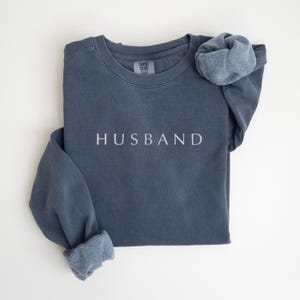 May include: A dark blue sweatshirt with the word "HUSBAND" embroidered in white on the front.