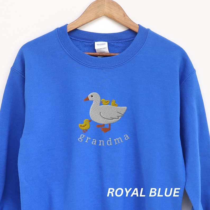 May include: Royal blue sweatshirt with an embroidered design of a white goose with yellow ducklings and the word "grandma" underneath.