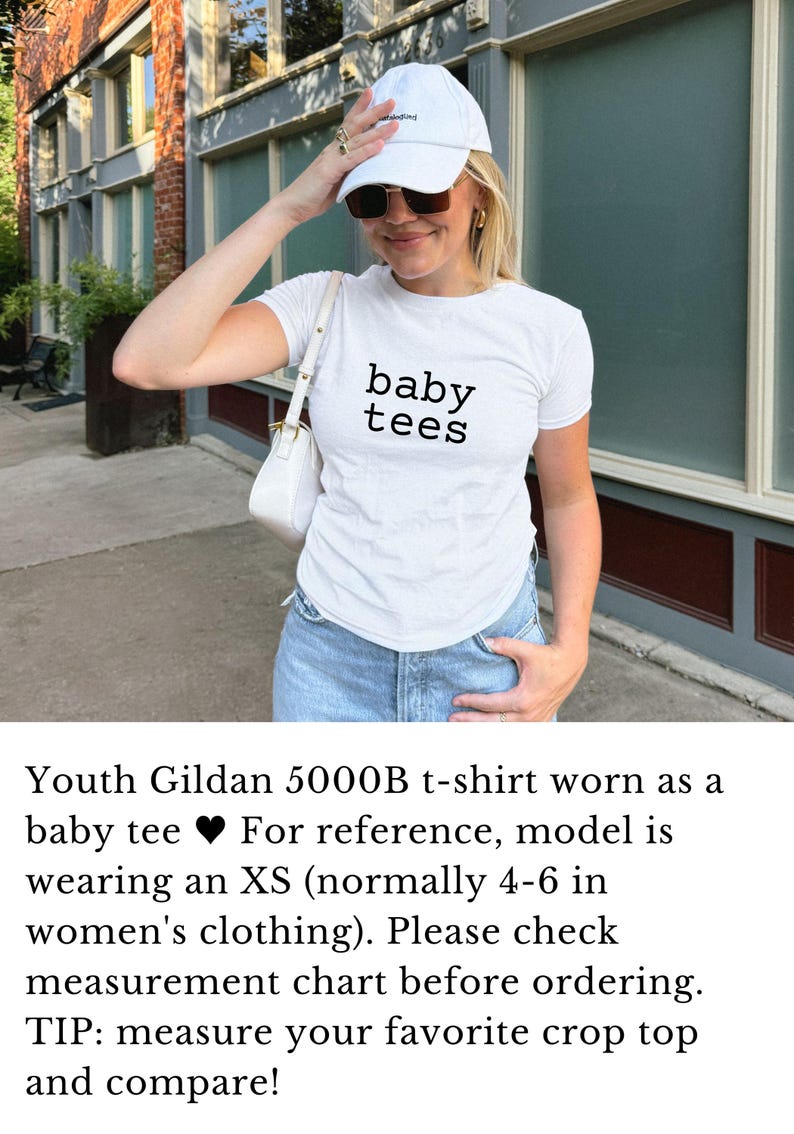 May include: White t-shirt with the text "baby tees" in black, paired with light-wash denim jeans. The model is wearing a white baseball cap and sunglasses. A white purse is worn over the shoulder.