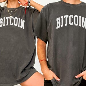 May include: Two gray t-shirts with the word "BITCOIN" printed in white on the front.