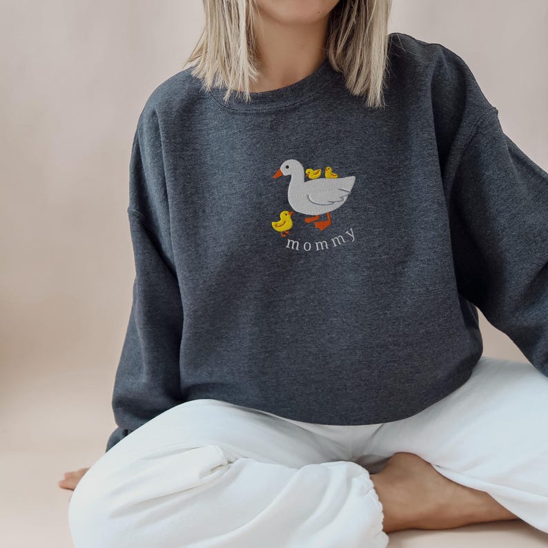 May include: A dark gray sweatshirt with a white goose and yellow ducklings embroidered on the front. The text "mommy" is embroidered below the goose.