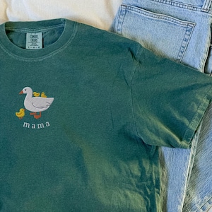 May include: A dark green t-shirt with an embroidered image of a goose and three ducklings. The text "mama" is embroidered below the image.