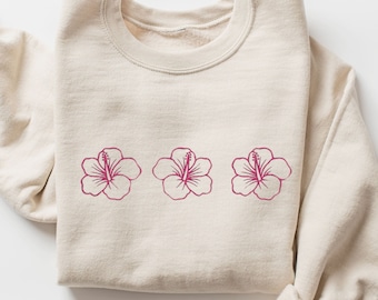 May include: A cream-colored sweatshirt with three pink hibiscus flowers printed on the front.