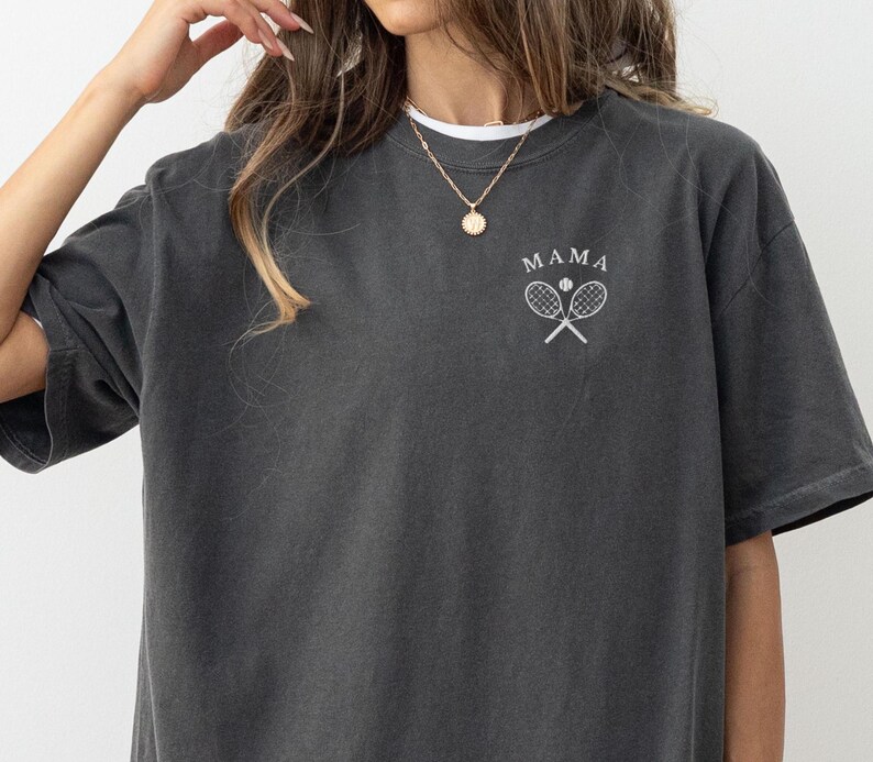 May include: A dark grey t-shirt with the word "MAMA" and a tennis racket graphic printed on the front.