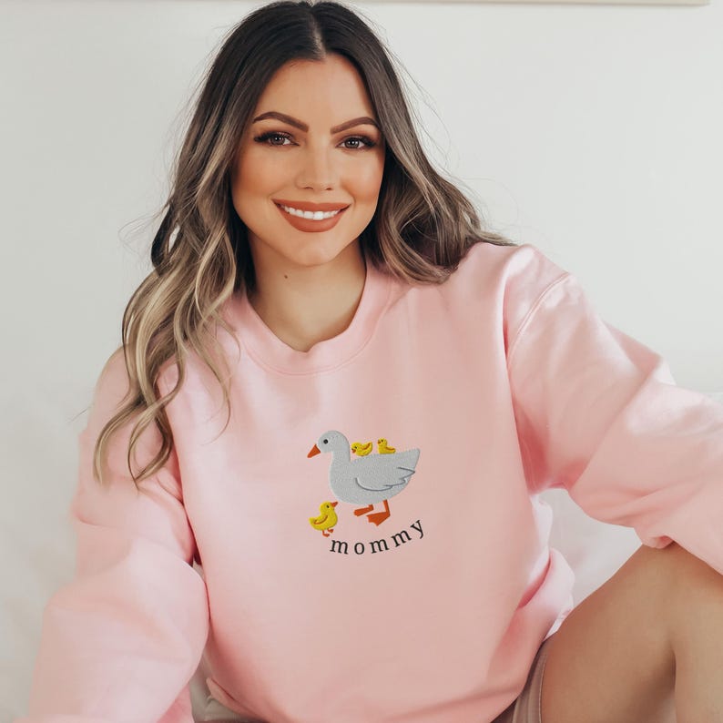 May include: A pink sweatshirt with a gray goose and yellow ducklings on it. The text "mommy" is printed below the goose.