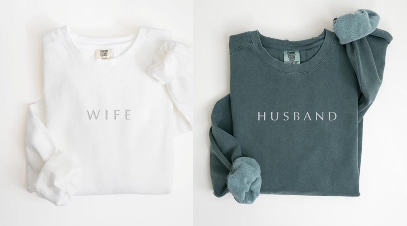 May include: Two long-sleeved shirts, one white with the word "WIFE" and one teal with the word "HUSBAND" printed on them.
