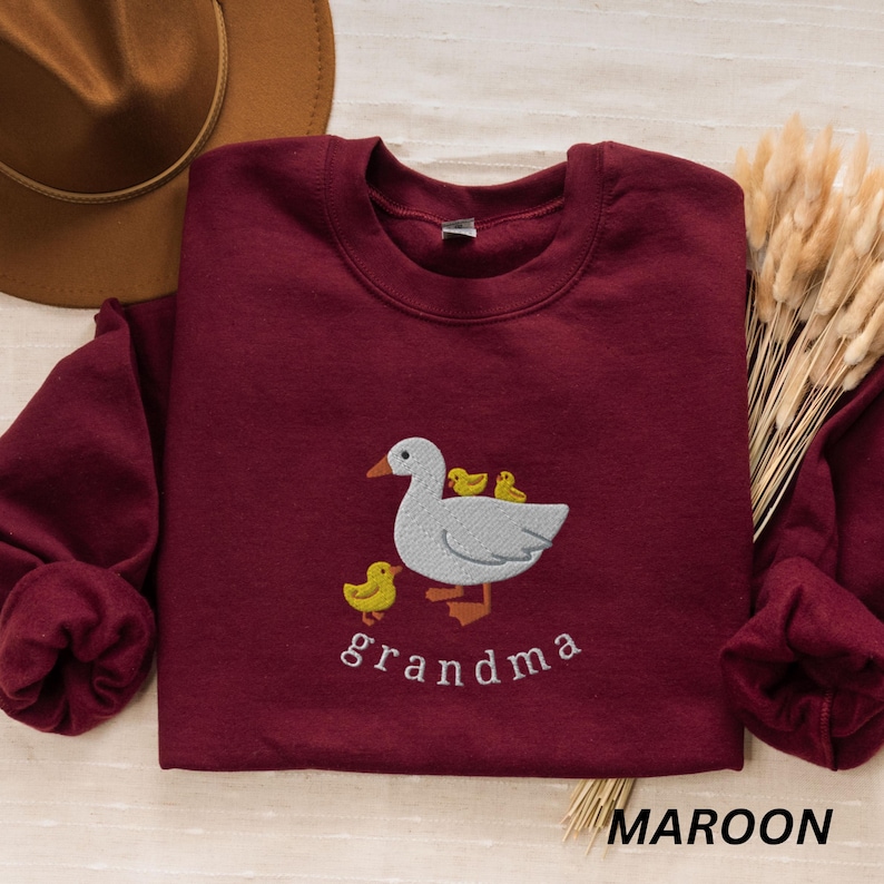 May include: A maroon sweatshirt with an embroidered design of a goose with three baby geese. The text "grandma" is embroidered below the goose.