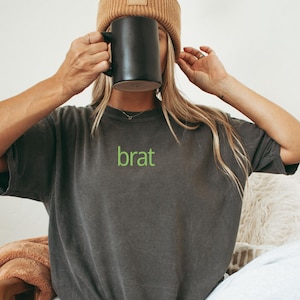 May include: A dark gray t-shirt with a green embroidered word "brat" on the front.