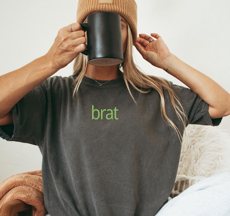 May include: A dark gray t-shirt with a green embroidered word "brat" on the front.