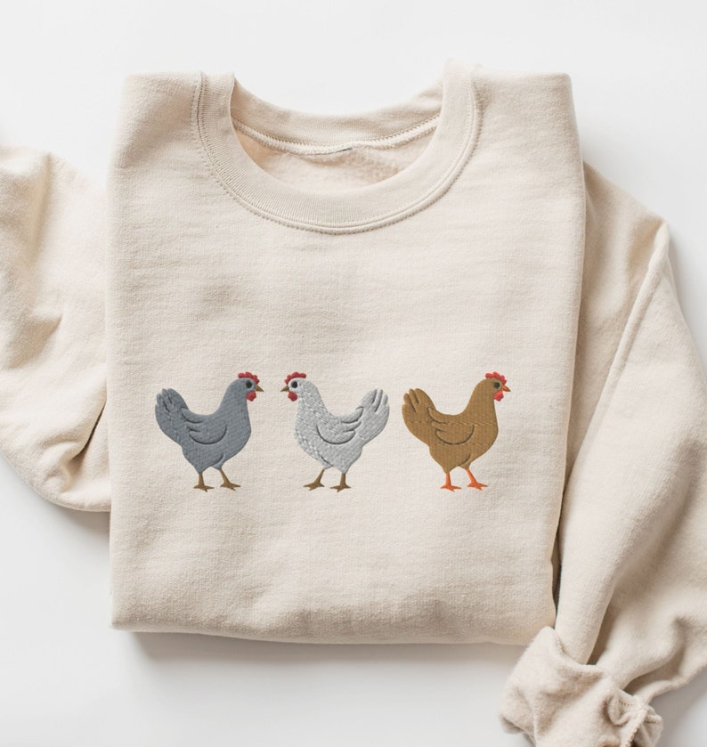May include: A beige sweatshirt with a graphic of three chickens in a row. The chickens are gray, white, and brown.