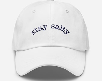 May include: White baseball cap with navy blue embroidery that reads "stay salty".