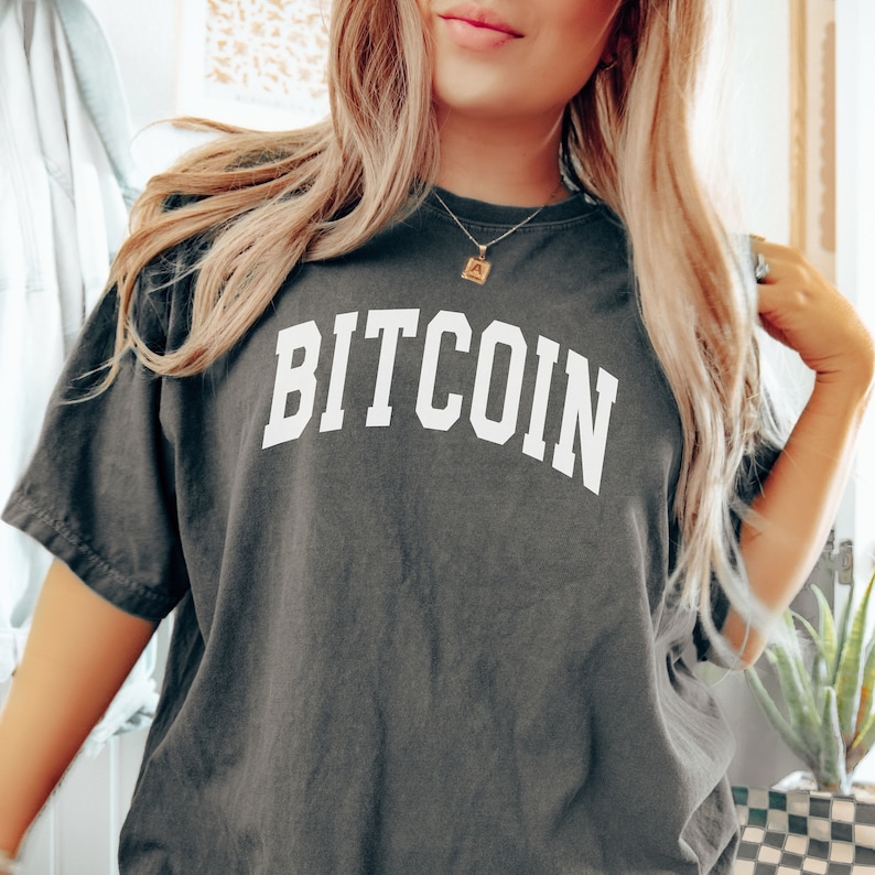 May include: A dark gray t-shirt with the word "BITCOIN" printed in white, in a collegiate font.