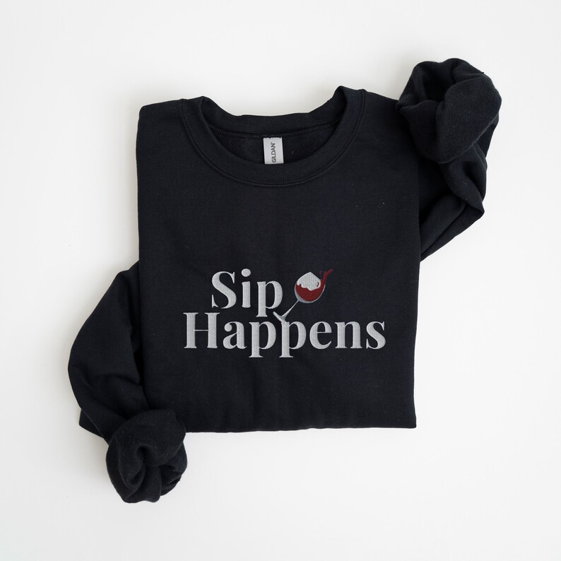 May include: Black sweatshirt with a white graphic that says "Sip Happens" and a red wine glass with a white rim.