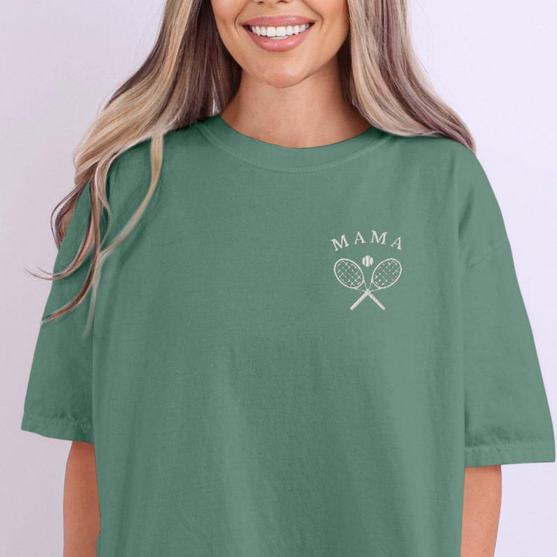 May include: A green t-shirt with the text "MAMA" and a graphic of two tennis rackets crossed with a tennis ball in the centre.
