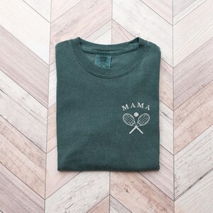 May include: A dark green t-shirt with the word "MAMA" and a white tennis racket and ball graphic.