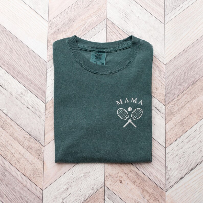 May include: A dark green t-shirt with the word "MAMA" and a white tennis racket and ball graphic.