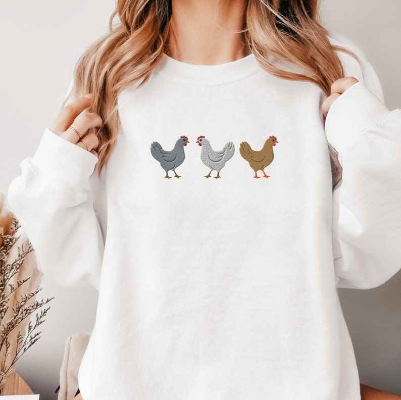 May include: White sweatshirt with a graphic of three chickens in a row. The chickens are gray, white, and brown.