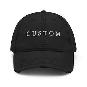 May include: Black distressed baseball cap with white embroidered text that reads "CUSTOM".