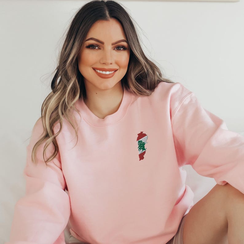 May include: A pink sweatshirt with an embroidered outline of Lebanon with the Lebanese flag colors inside.