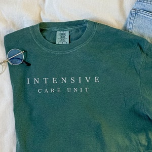 May include: A dark green long-sleeved t-shirt with the text "INTENSIVE CARE UNIT" printed in white on the front.