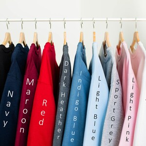 K&ouml;nnte beinhalten: Zehn verschiedene farbige Sweatshirts h&auml;ngen an einem Gestell. Die Farben sind Schwarz, Marine, Rotbraun, Rot, Dunkelgrau meliert, Indigo, Hellblau, Sportgrau, Rosa und Wei&szlig;.