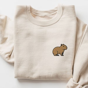 May include: A beige sweatshirt with a brown capybara embroidered on the front.